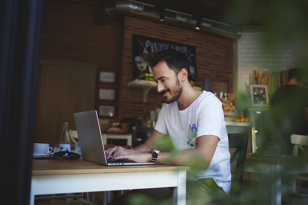 Jovem com laptop estudando em um curso de Marketing EaD dentro de cafeteria