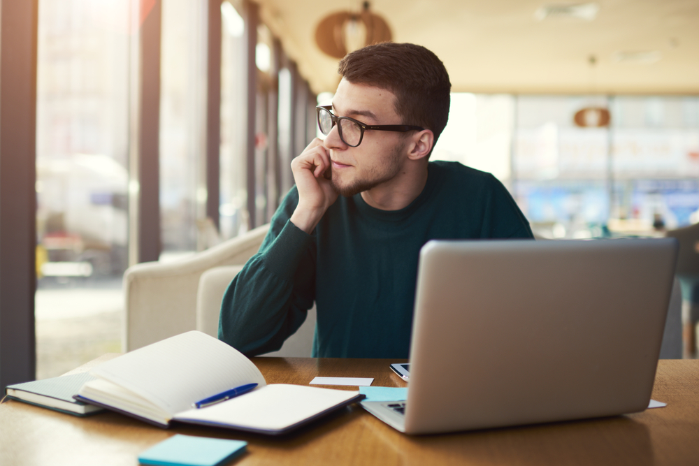 Estudante da modalidade EaD pensativo, de frente a um laptop