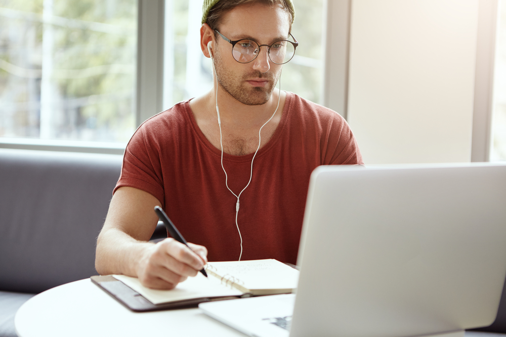 Homem jovem em frente a um laptop estudando e fazendo uma graduação EaD